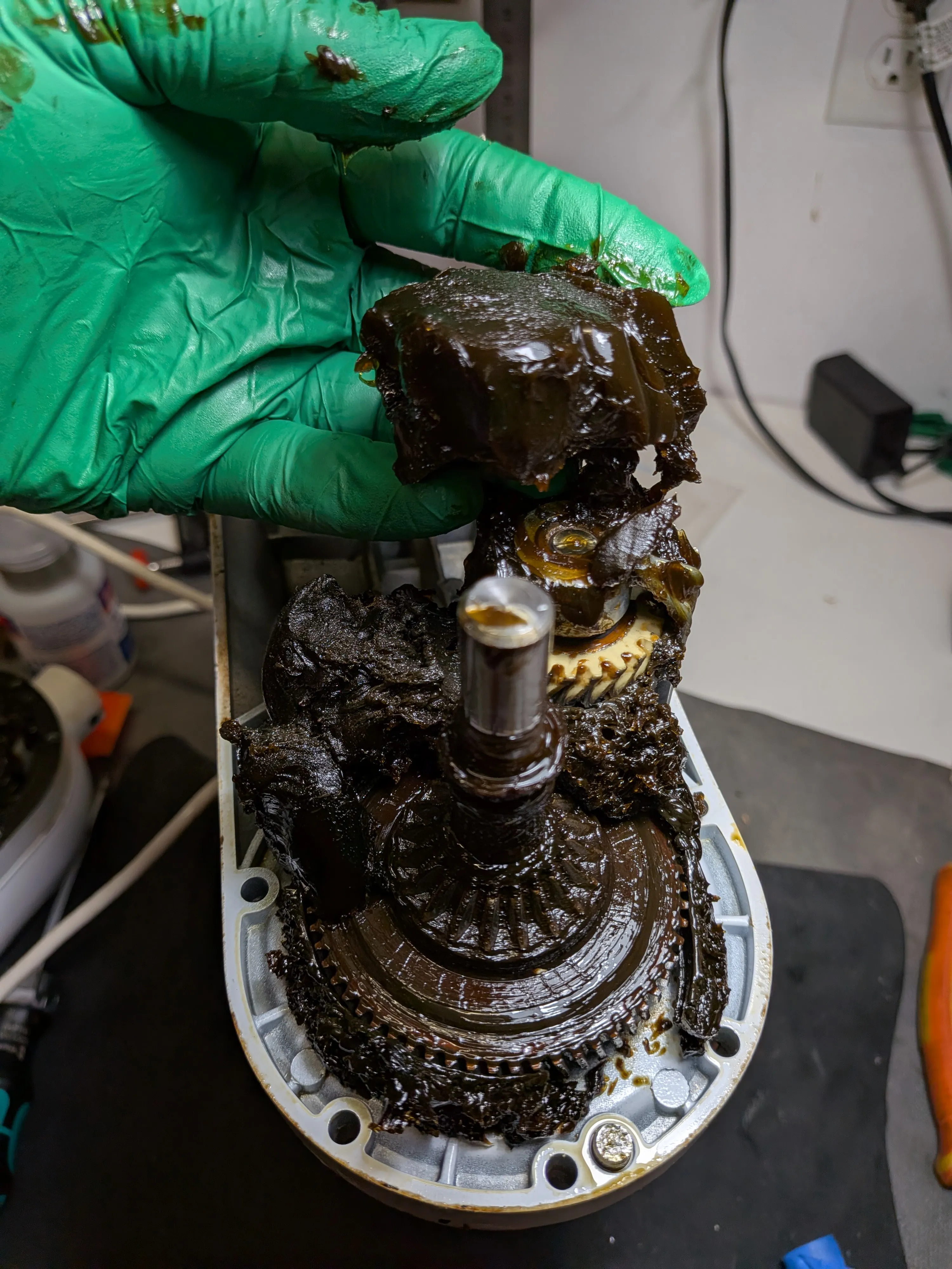 A gloved hand lifting a clump of old blackened grease out of an opened tilt-head KitchenAid mixer